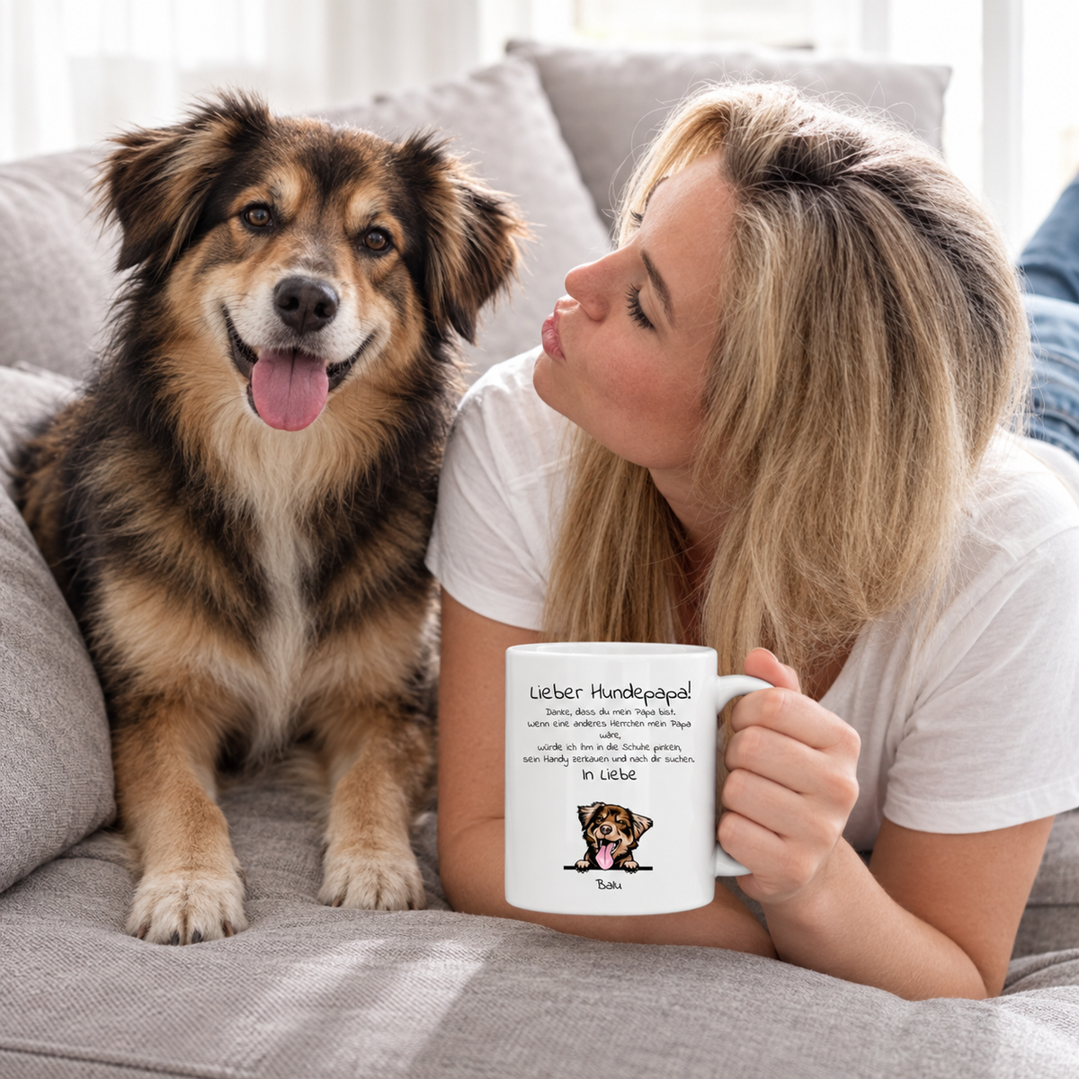 Frau mit personalisierter Tasse „Lieber Hundepapa“ und Hund auf einem grauen Sofa. Tasse ist weiß mit Text und Illustration.