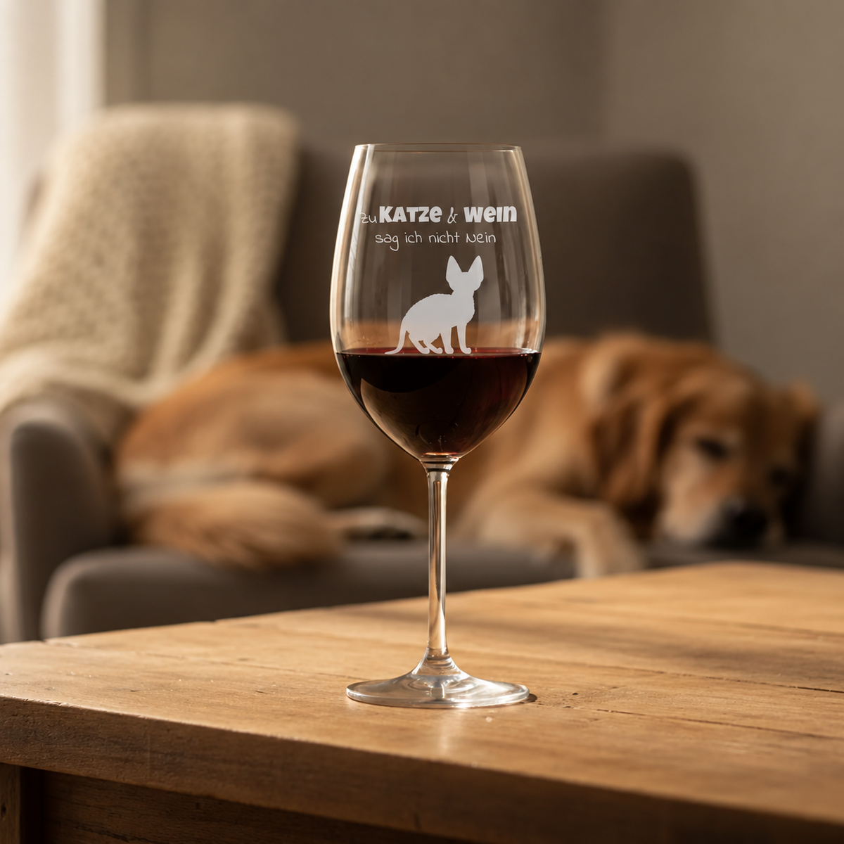 Personalisiertes Weinglas mit graviertem Spruch und Katze, gefüllt mit Rotwein auf einem Holztisch.