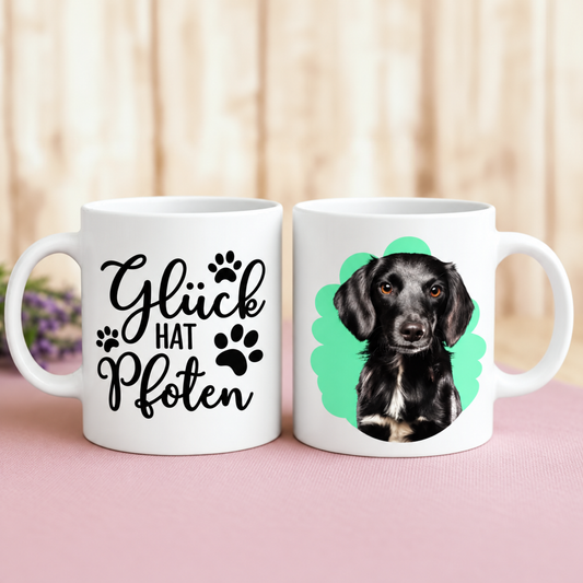 Weiße Tasse mit schwarzem Hundeporträt und der Aufschrift "Glück hat Pfoten".