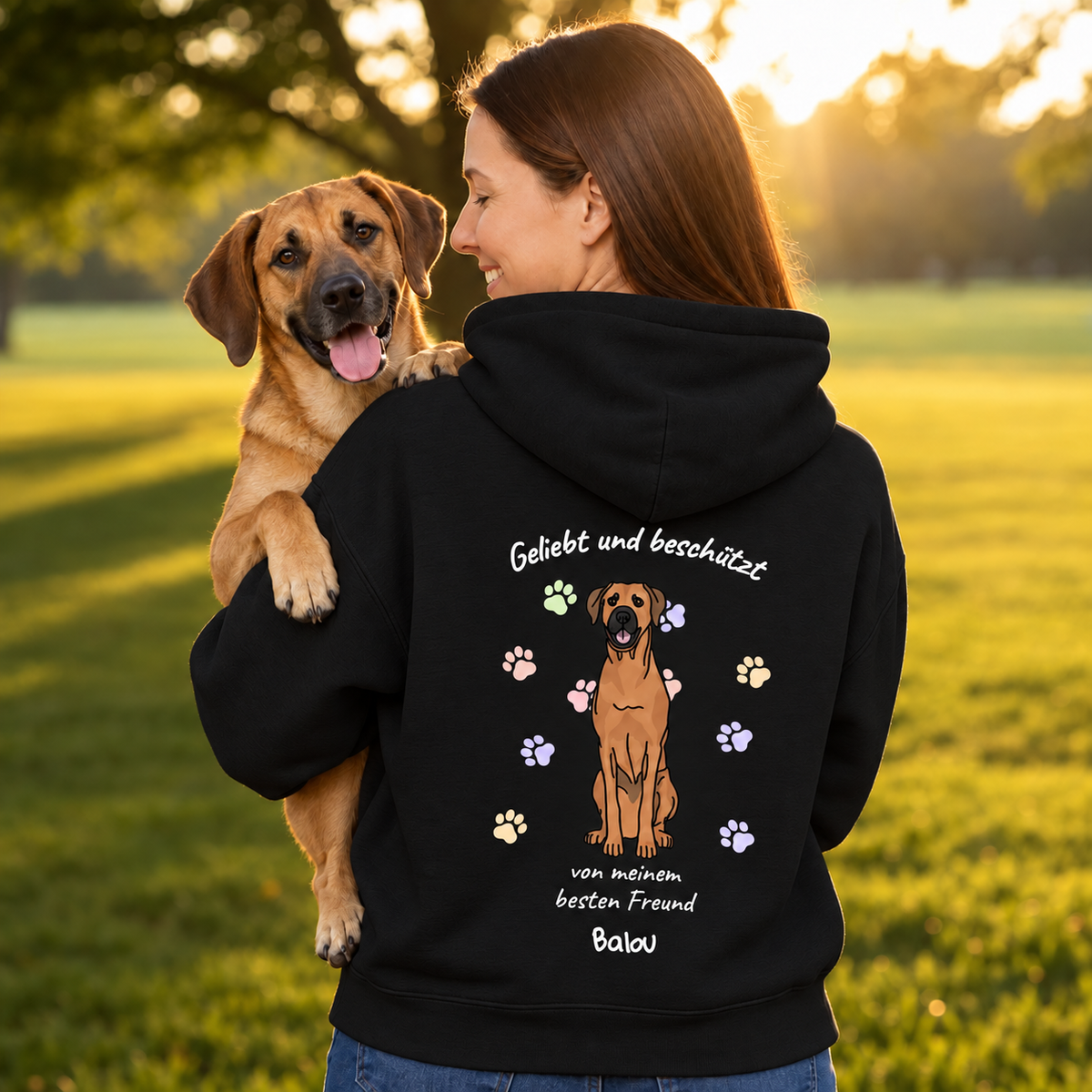 Schwarzer Hoodie mit Aufdruck "Geliebt und beschützt" und Illustration eines Hundes, getragen von einer Frau mit Hund.