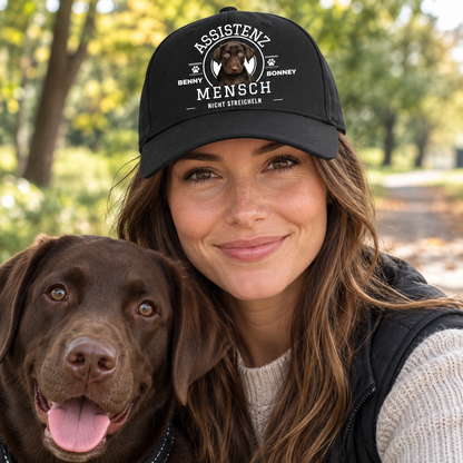 Personalisierte schwarze Cap mit Aufdruck „Assistenz Mensch - nicht streicheln“ und Hundebild. Frau mit Hund lächelt.