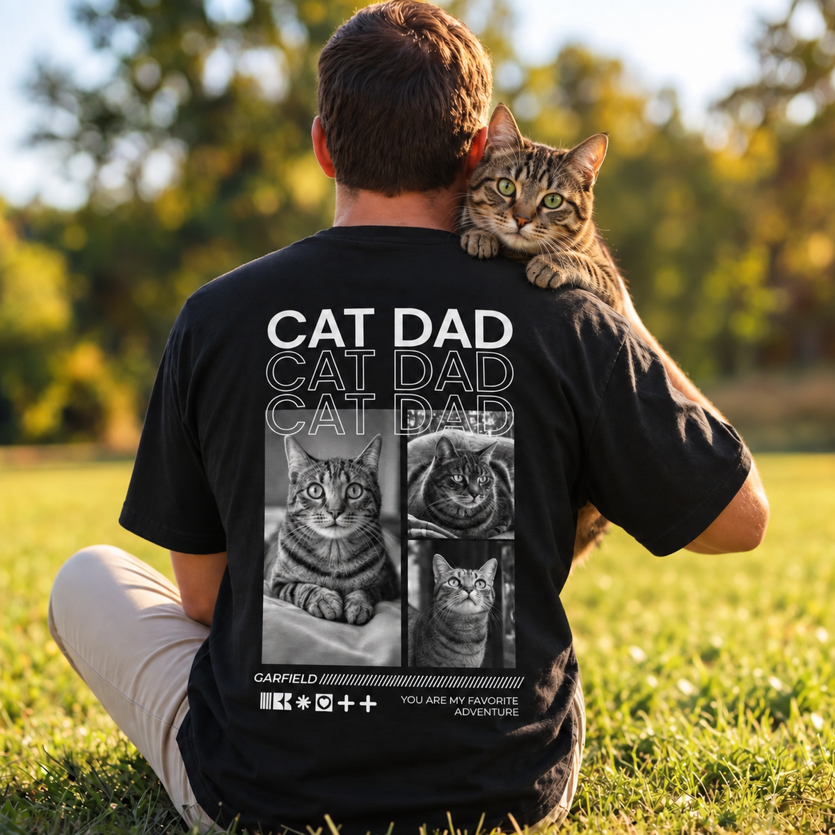 Schwarzes T-Shirt mit dem Aufdruck "Cat Dad" und Katzenmotiven, getragen von einer Person mit einer Katze.