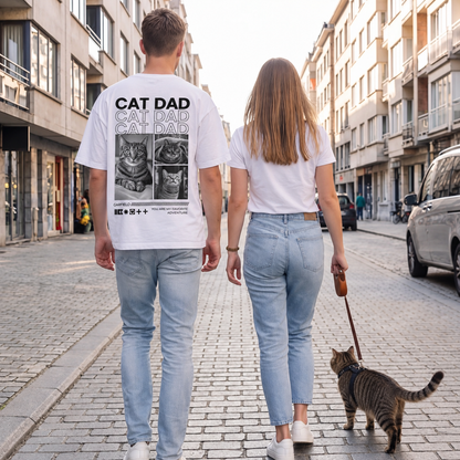 Weißes T-Shirt mit Katzendruck auf dem Rücken, zwei Personen und eine Katze beim Spazieren in einer Stadtstraße.