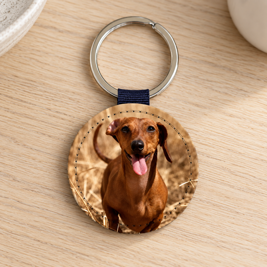 Runder Schlüsselanhänger mit Foto eines lächelnden Hundes auf einem Holztisch.