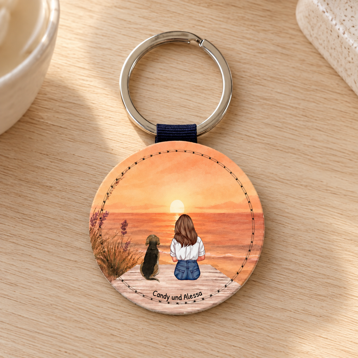 Personalisierter runder Schlüsselanhänger mit einer Illustration von einer Frau und einem Hund beim Sonnenuntergang.
