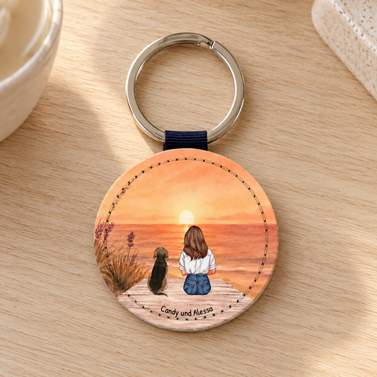 Personalisierter runder Schlüsselanhänger mit einer Illustration von einer Frau und einem Hund beim Sonnenuntergang.