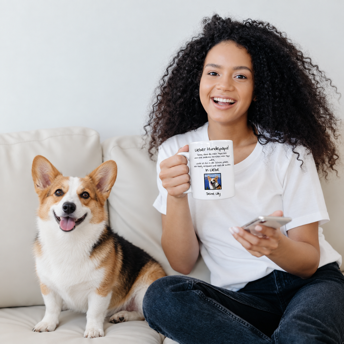 Person hält eine personalisierte Tasse mit Aufschrift „Lieber Hundepapa“ und Foto, sitzt auf einem Sofa neben einem Hund.