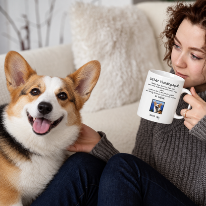 Person trinkt aus weißer Tasse mit "Lieber Hundepapa"-Aufdruck, koranischer Hund sitzt neben ihr.