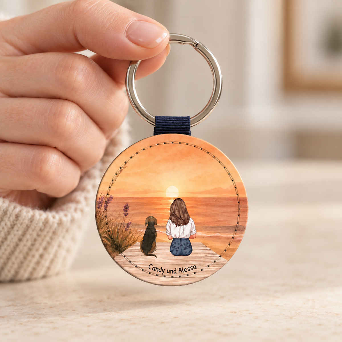 Personalisierter runder Schlüsselanhänger mit Illustration einer Person und Hund am Meer bei Sonnenuntergang.
