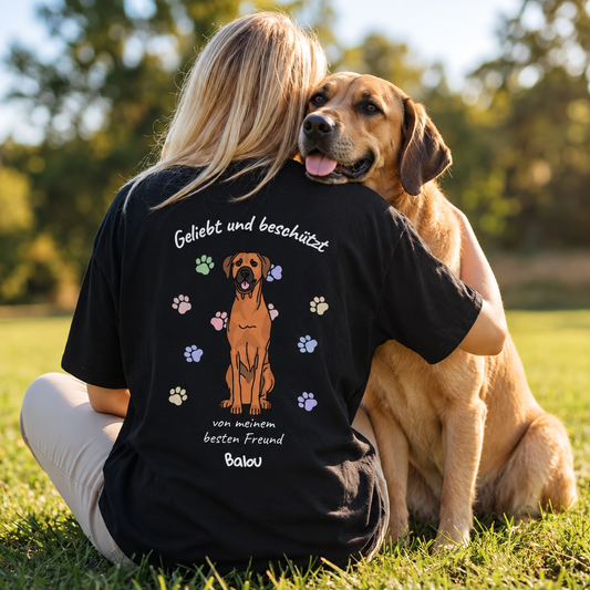 Schwarzes T-Shirt mit dem Aufdruck "Geliebt und beschützt" sowie einem Hund und bunten Pfotenabdrücken.