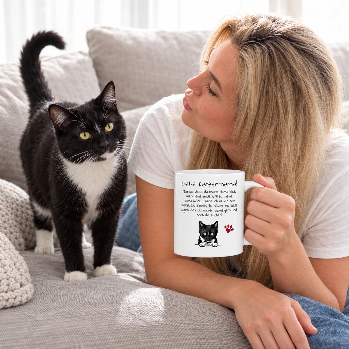Person trinkt aus einer weißen Tasse mit Katzenmotiv und schwarzer Katze auf dem Boden.