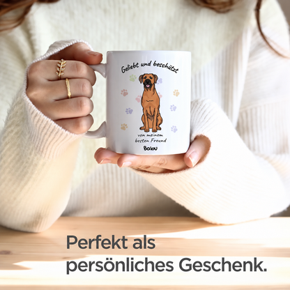 Weiße Tasse mit Aufdruck eines Hundes und den Worten "Geliebt und beschützt" sowie personalisierbarem Namen.