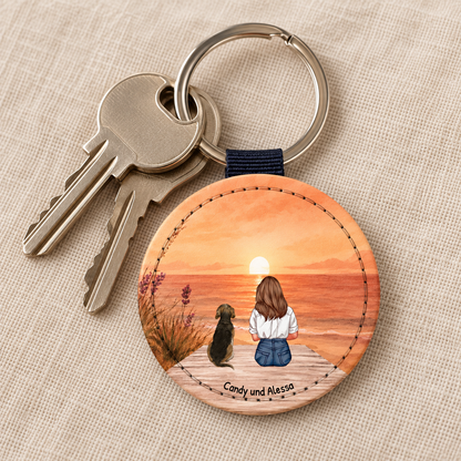 Personalisierter Schlüsselanhänger mit abgebildeter Person und Hund bei Sonnenuntergang. Holzkreis mit Gravur.