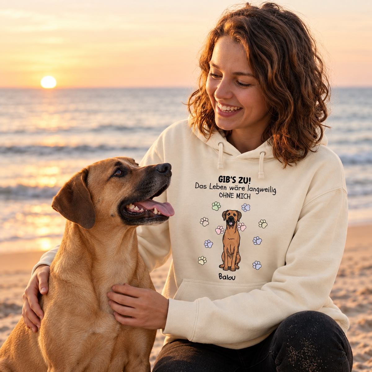 Beige Hoodie mit Druckmotiv „Das Leben wäre langweilig ohne mich“ und Hundemotiv. Frau sitzt am Strand mit Hund.