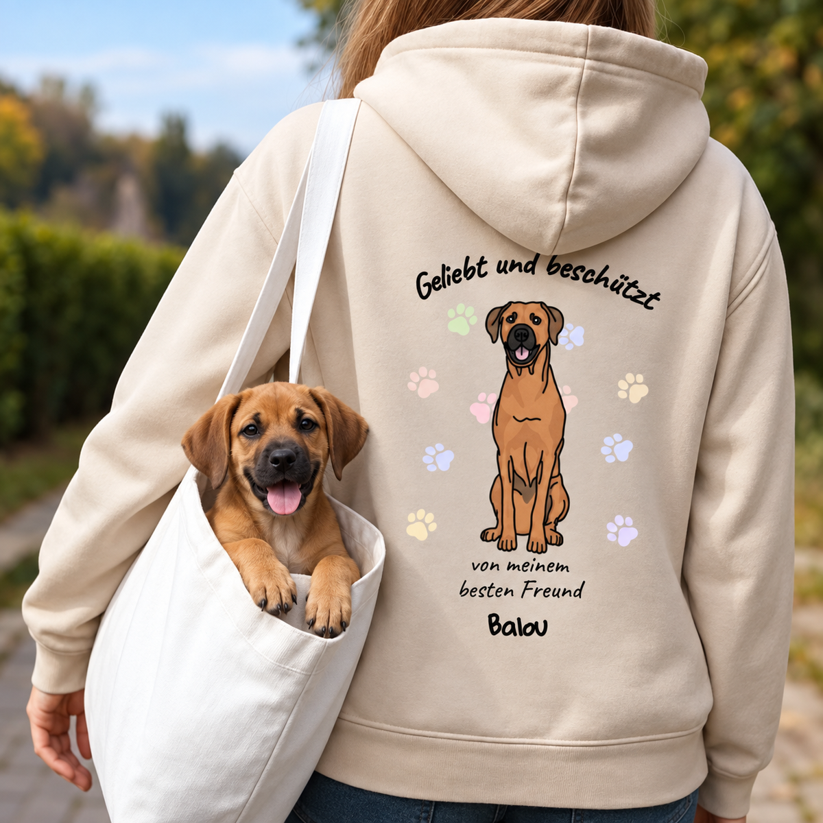Hoodie in Beige mit Aufdruck „Geliebt und beschützt“ und Hundemotiv auf der Rückseite. Kleine Hundewelpe in Tragetasche.