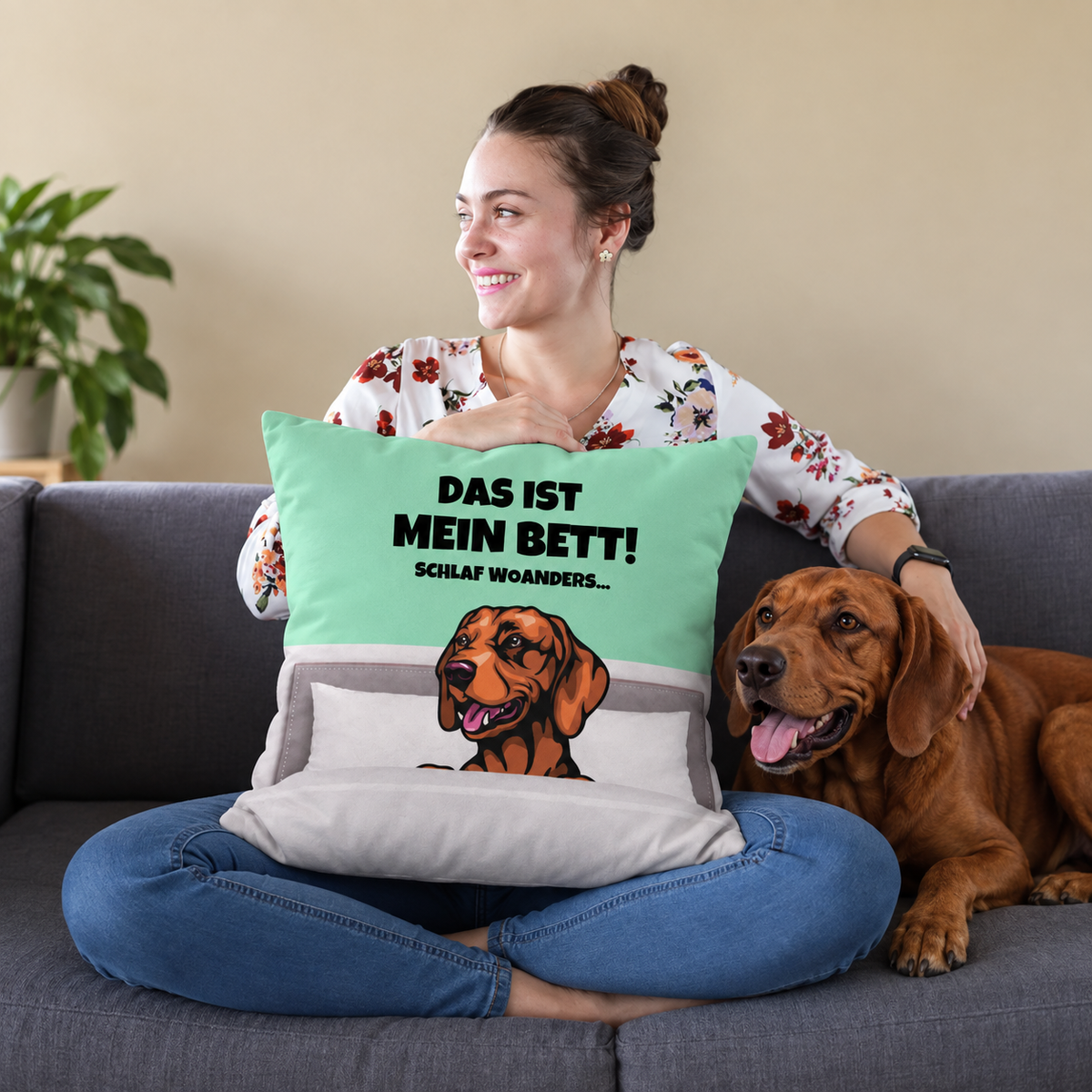 Personalisiertes Kissen mit Hundemotiv und Text, in mintgrün und grau, auf einem Sofa mit einer Frau und einem Hund.