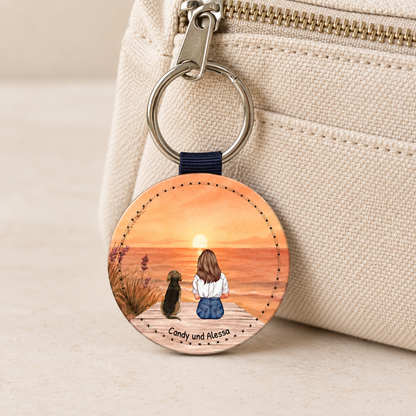 Personalisierter Schlüsselanhänger mit Illustration einer Frau und einem Hund vor einem Sonnenuntergang.