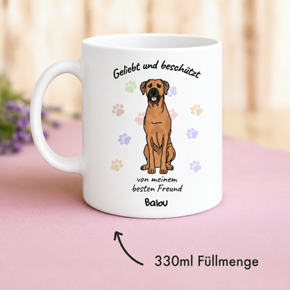Personalisierte Keramiktasse in Weiß mit Druck eines Hundes und dem Text "Geliebt und beschützt". Füllmenge 330 ml.
