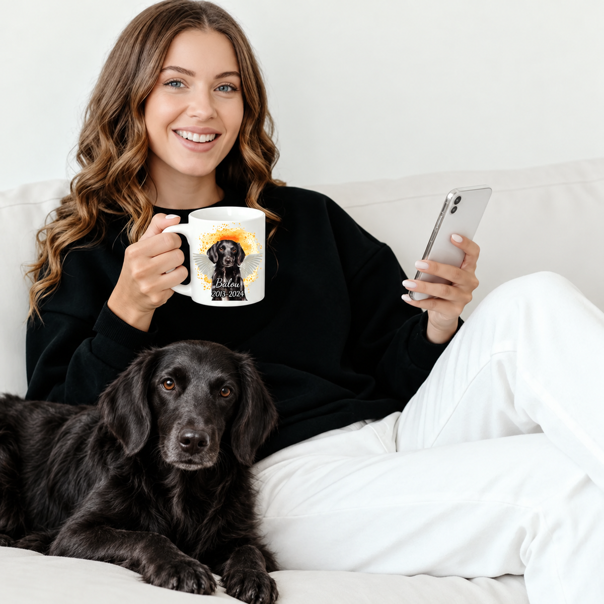 Person trinkt aus einer personalisierten Tasse mit Haustierportrait und hält ein Smartphone, daneben ein schwarzer Hund.