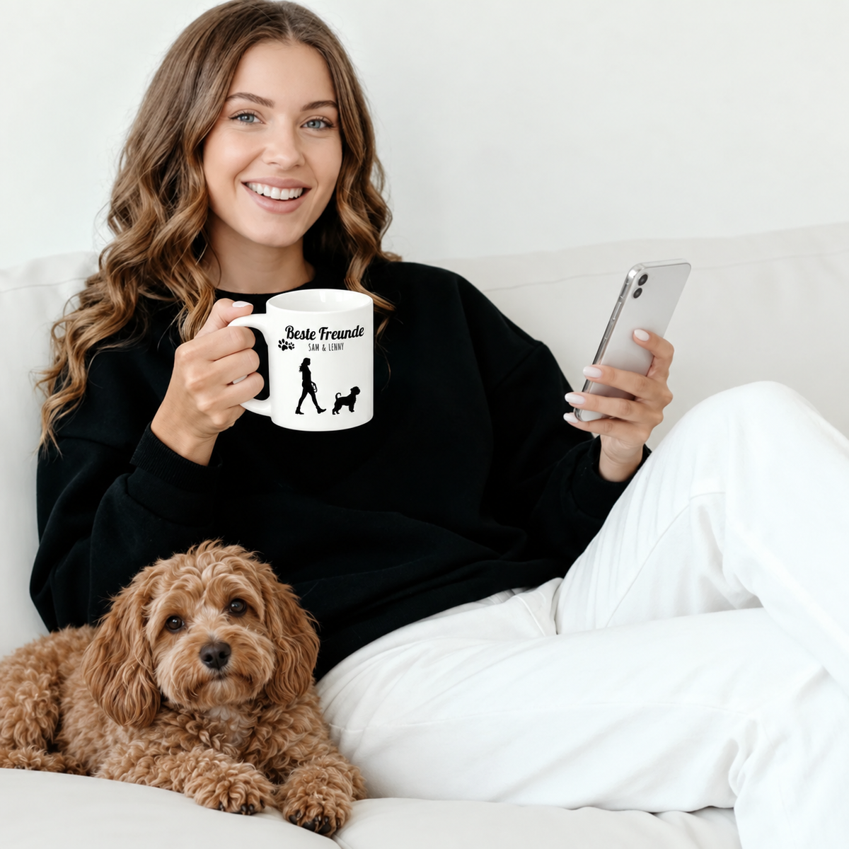 Person hält eine personalisierte weiße Tasse mit Aufdruck und sitzt auf dem Sofa neben einem Hund.