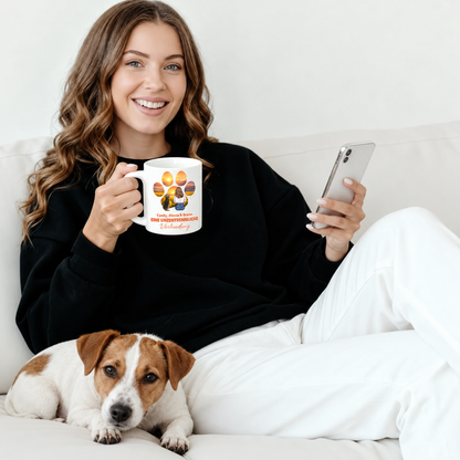 Personalisierte Tasse mit buntem Pfotenabdruck und Schriftzug, gehalten von einer Frau auf der Couch mit Hund.