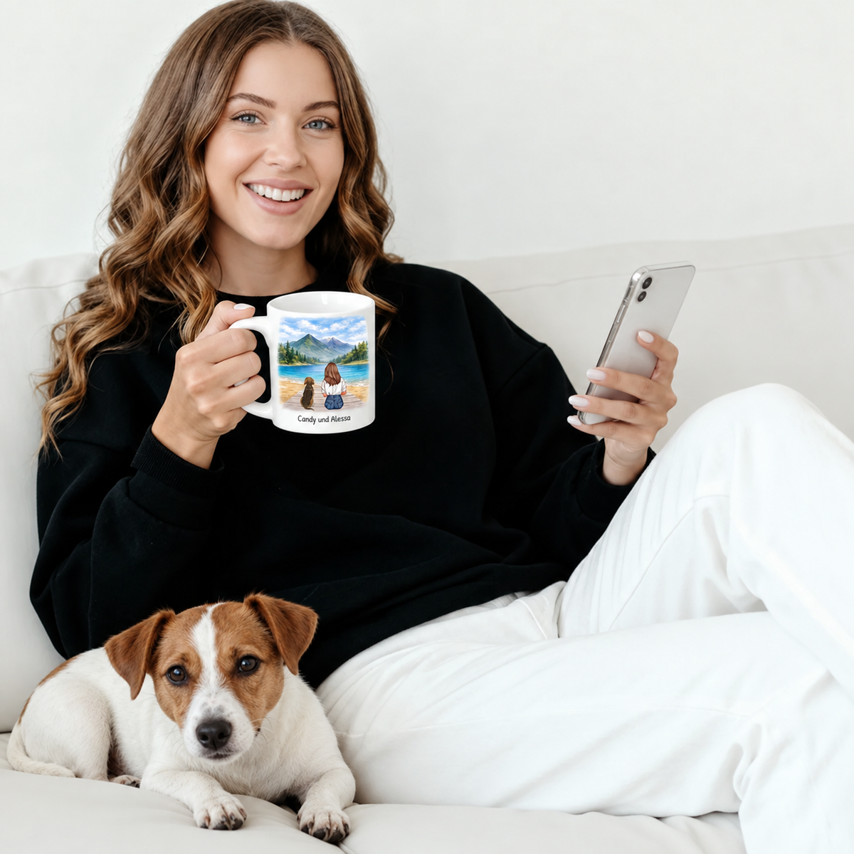 Person hält eine personalisierte Tasse mit Landschaftsmotiv, neben ihr liegt ein Hund auf der Couch.