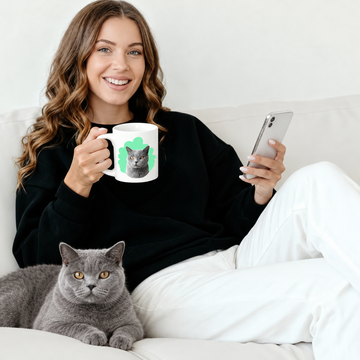 Person sitzt auf einem Sofa und hält eine personalisierte Tasse mit Katzenportrait, neben ihm eine graue Katze.