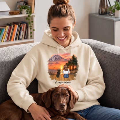 Beige Hoodie mit personalisiertem Druck einer Frau und Hund vor einem Sonnenuntergang, sitzend auf Sofa mit Hund.