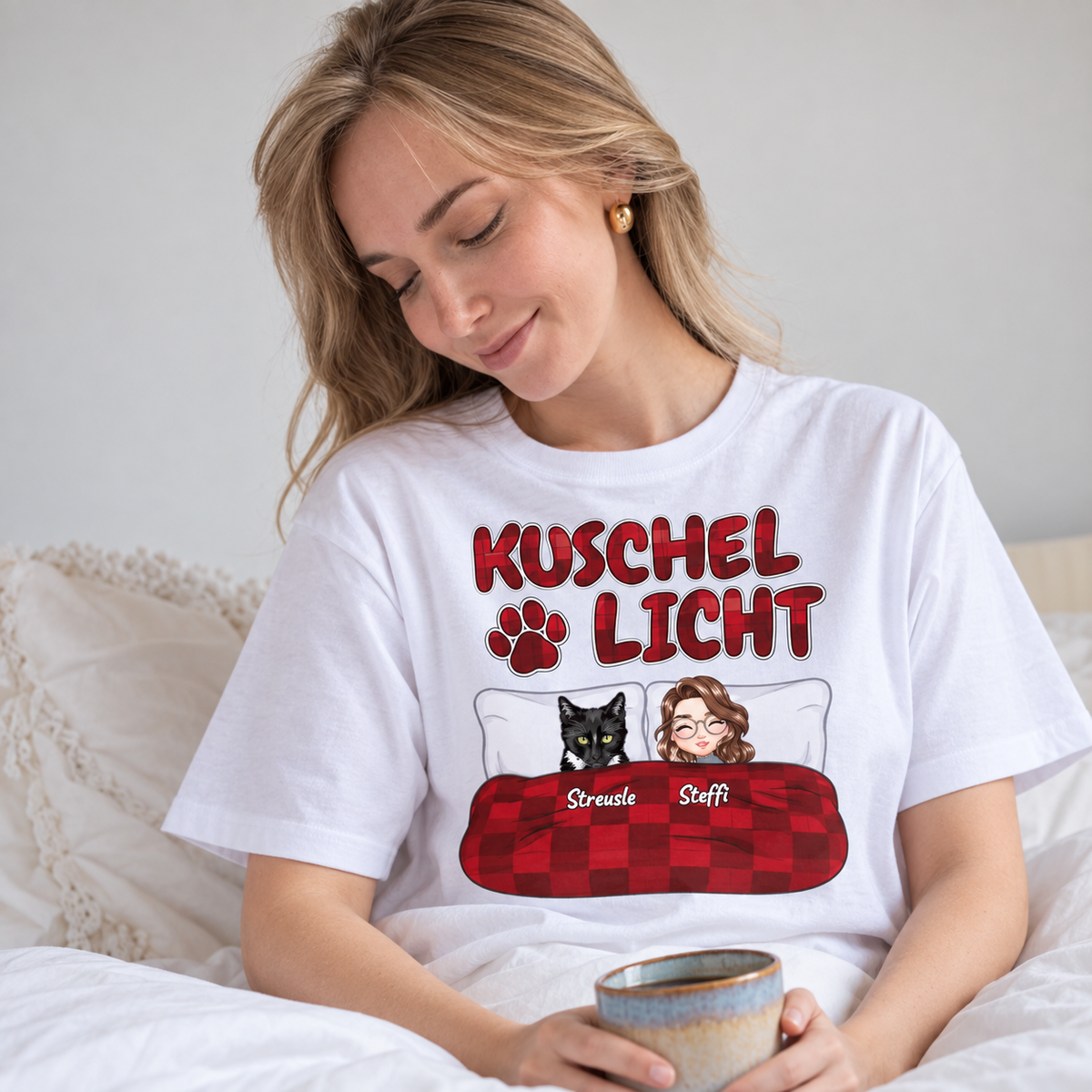 Weißes T-Shirt mit dem Aufdruck "Kuschel Licht" und Illustrationen einer Frau und einer Katze im Bett.