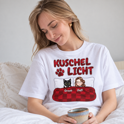 Weißes T-Shirt mit dem Aufdruck "Kuschel Licht" und Illustrationen einer Frau und einer Katze im Bett.