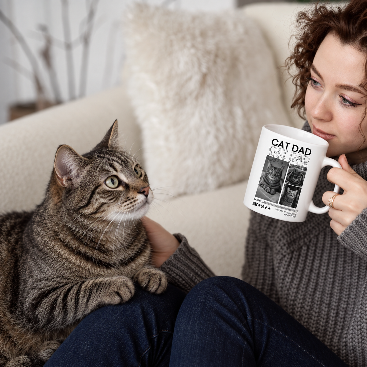 Person mit personalisierter Tasse "Cat Dad" und Katze auf einem hellen Sofa. Tasse weiß mit Bildern von Katzen.