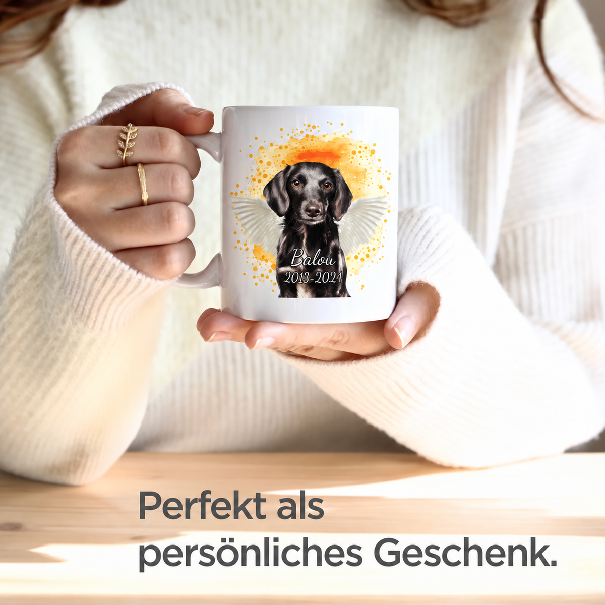 Weiße Tasse mit Haustierporträt eines Hundes, goldenen Akzenten und Text. In Händen einer Person mit Langarm-Oberteil.