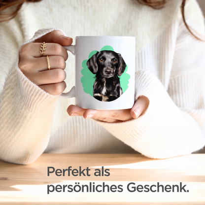 Person hält eine personalisierte weiße Tasse mit einem Hundeportrait in einem grünen Hintergrund.