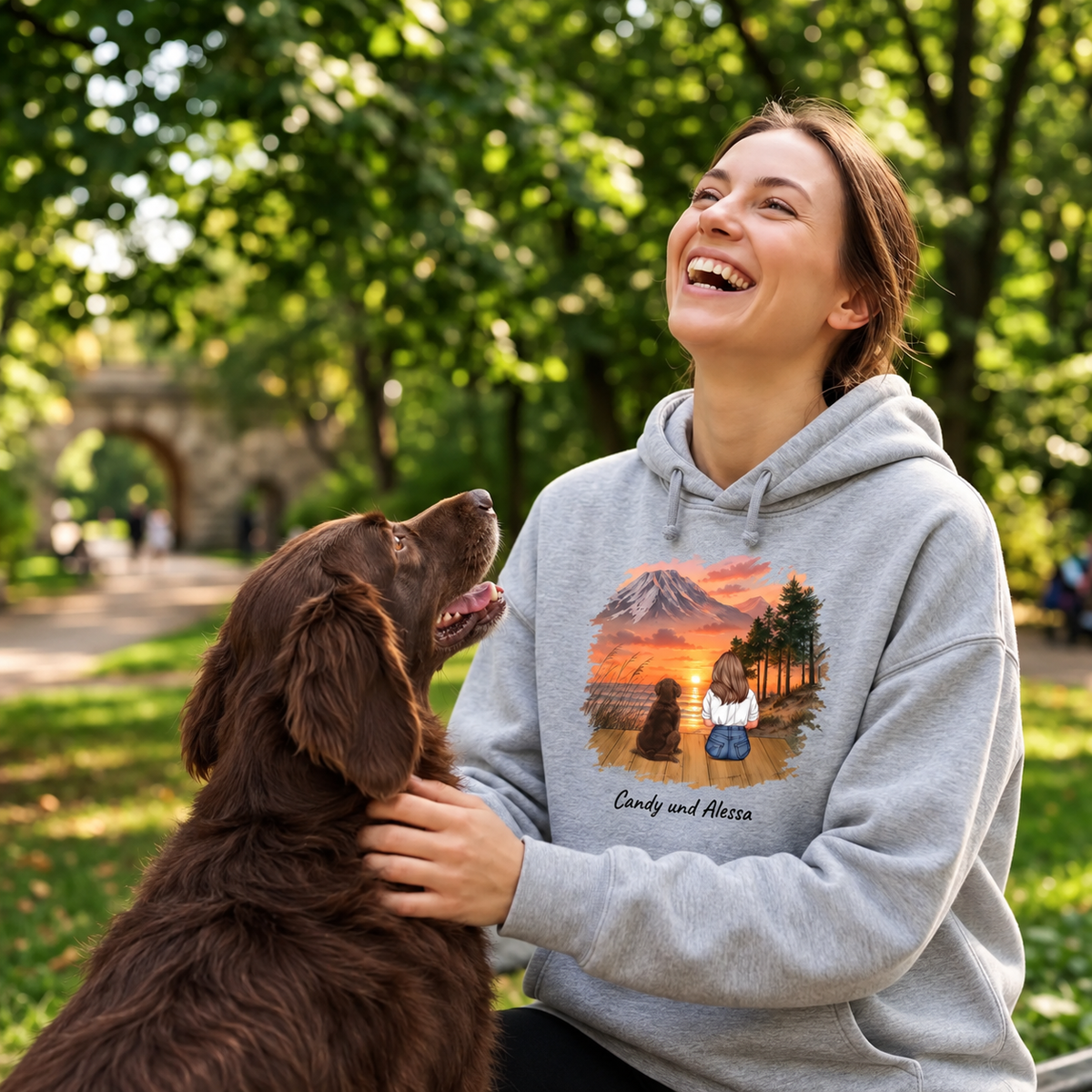 Grauer Hoodie mit personalisiertem Druck einer Landschaft und zwei Tieren, getragen von einer lächelnden Frau.