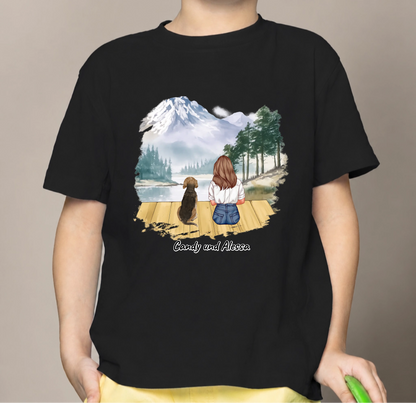 Schwarzfarbiges Kinder T-Shirt mit Grafik eines Mädchens und Hund am See mit Bergen im Hintergrund.