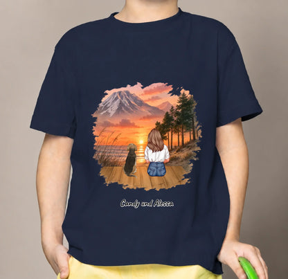 Blaues Kinder T-Shirt mit Grafik von sitzender Person und Hund vor sunset Landschaft.