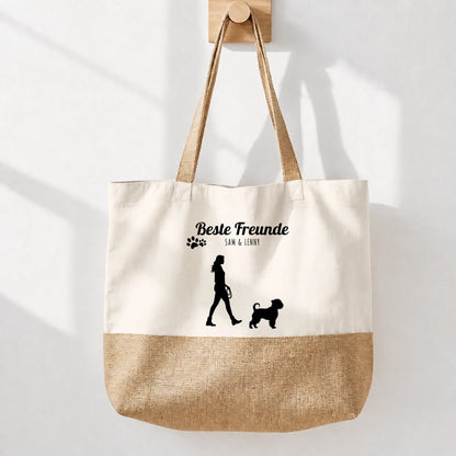 Stoff-Einkaufstasche in Beige mit Jute-Boden und schwarzem Aufdruck „Beste Freunde“. Silhouette einer Person mit Hund.