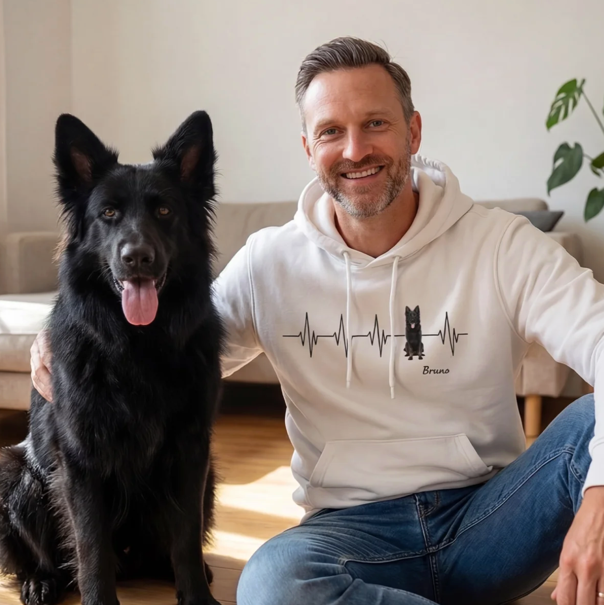 Weißer Hoodie mit Herzschlag-Muster und Hundemotiv, sitzender Mann neben schwarzem Hund.