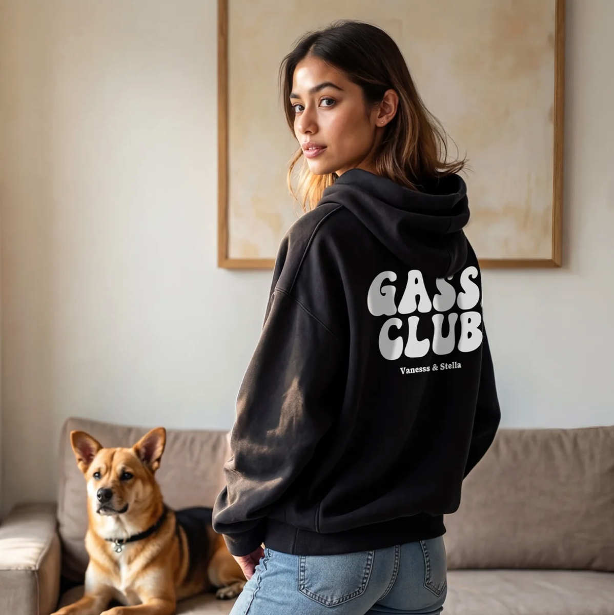 Schwarzer Hoodie mit "GASS CLUB" Aufdruck auf dem Rücken, Person steht mit Hund in modernem Wohnzimmer.