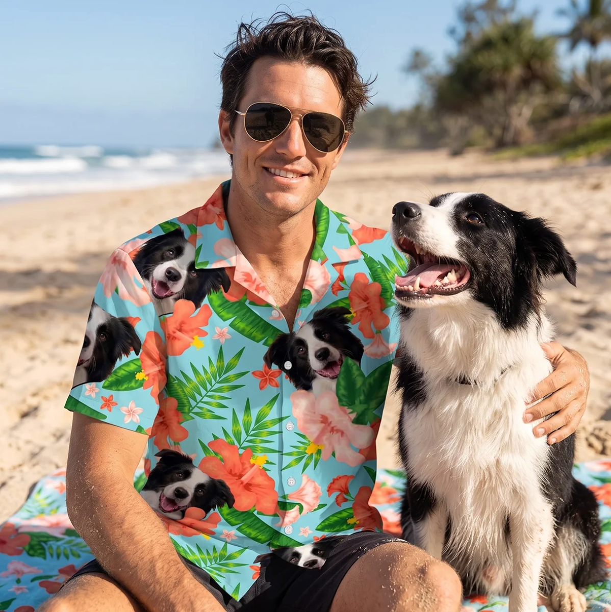 Mann mit Sonnenbrille trägt ein personalisiertes Hawaiihemd mit Hundemotiven, sitzt am Strand neben einem Hund.