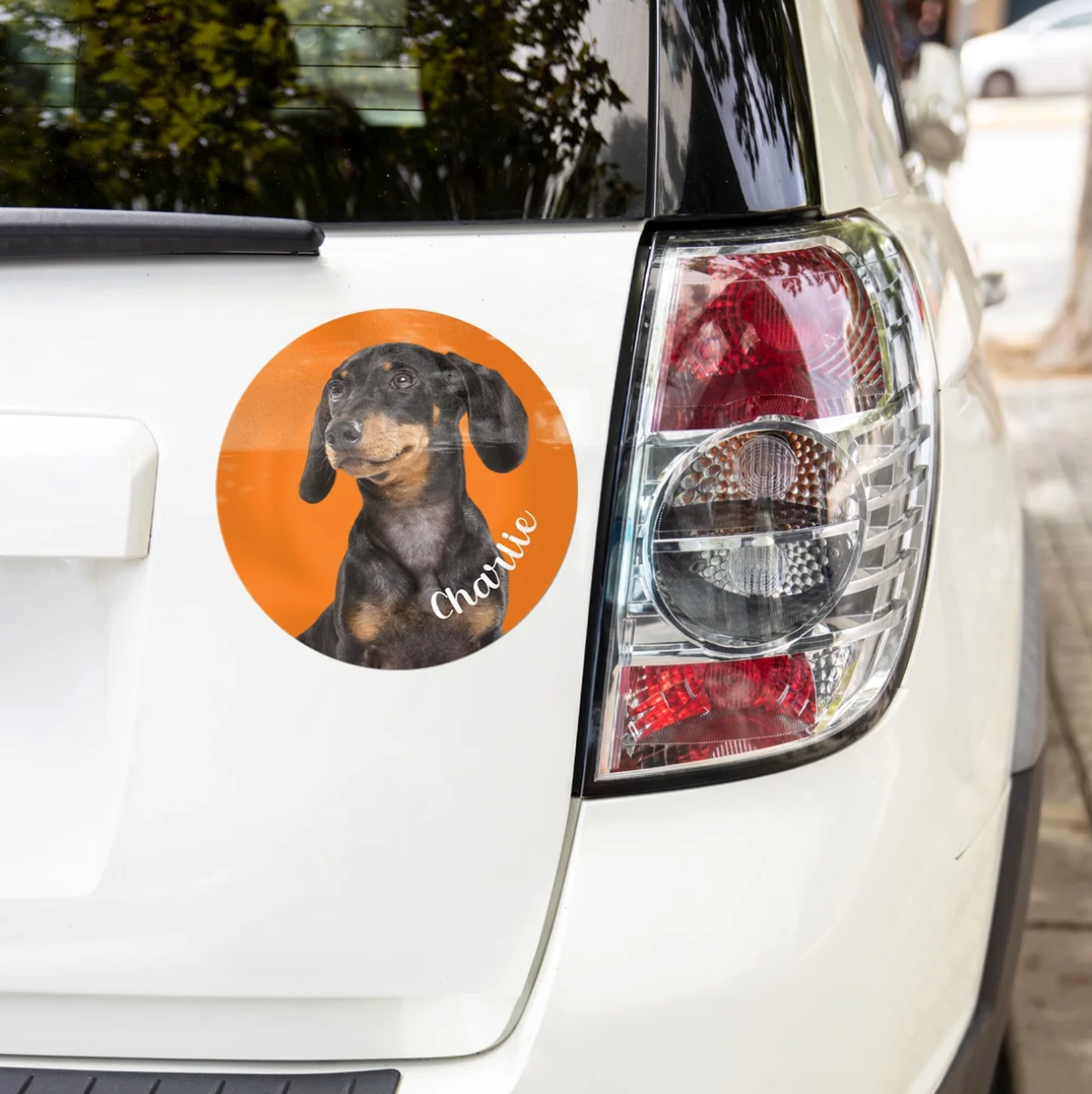Personalisierter Autoaufkleber mit Bild eines Dackels auf orangefarbenem Hintergrund, befestigt an einem weißen Auto.