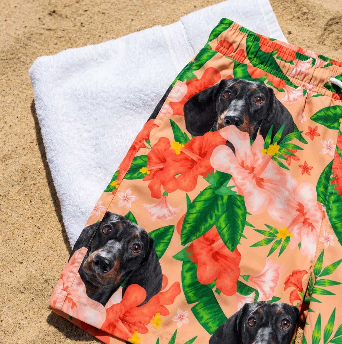 Personalisierte Badehose mit floralen Motiven und Hundedruck auf einem Sandstrand liegend.