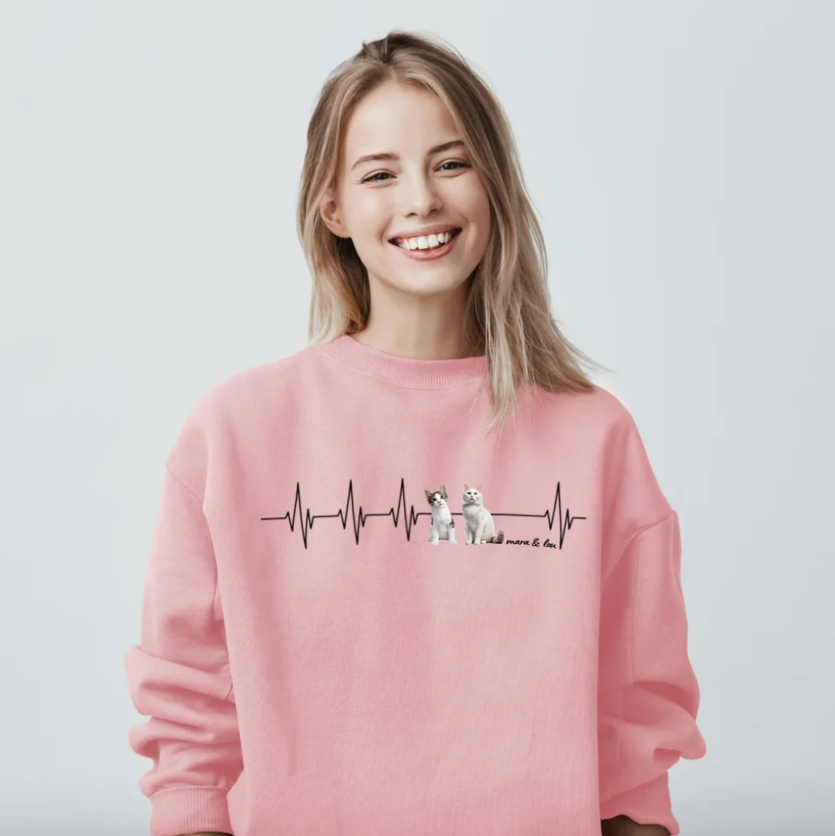 Rosa Sweatshirt mit Herzschlag-Motiv und Tierillustrationen. Trägerin lächelt.