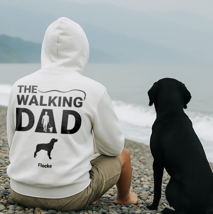 Weißer Hoodie mit Rückendruck "THE WALKING DAD" und Hundemotiv, getragen von sitzendem Mann am Strand.