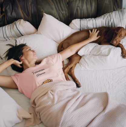 Frau in pinkem T-Shirt liegt auf dem Bett neben einem Hund, umgeben von Kissen und einer Decke.