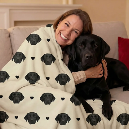 Personalisierte Decke mit schwarzen Hundeköpfen auf beigem Hintergrund, umhüllt eine lächelnde Frau.