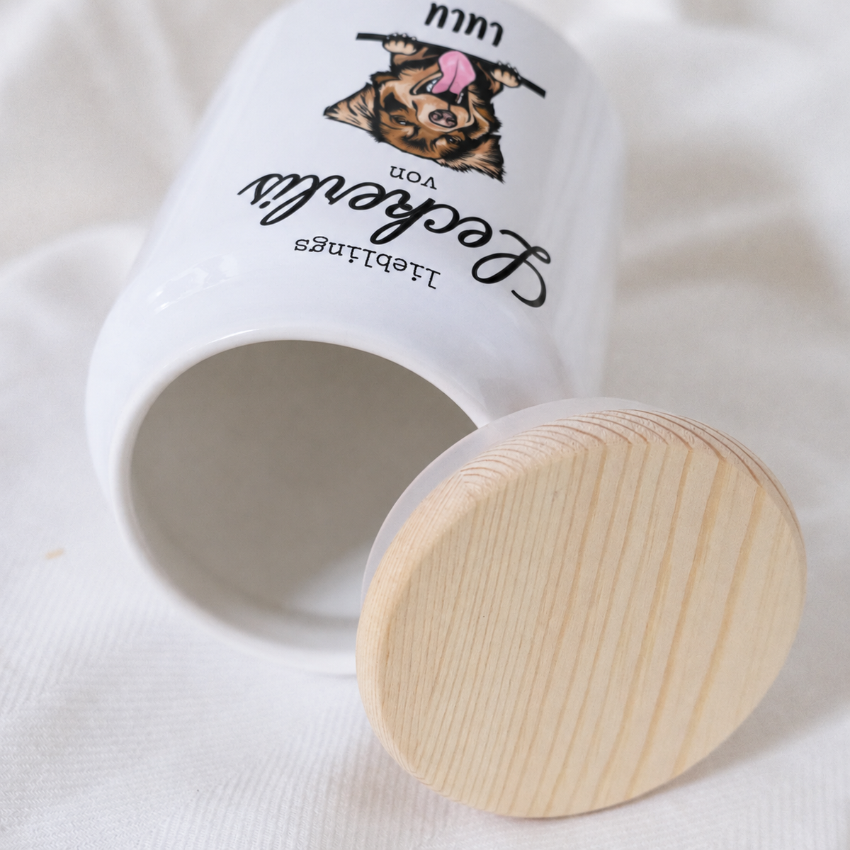 Personalisierte Leckerlidose aus weißem Keramik mit Holzdeckel, mit Hundemotiv und dem Text „Lieblings Leckerli von...“.