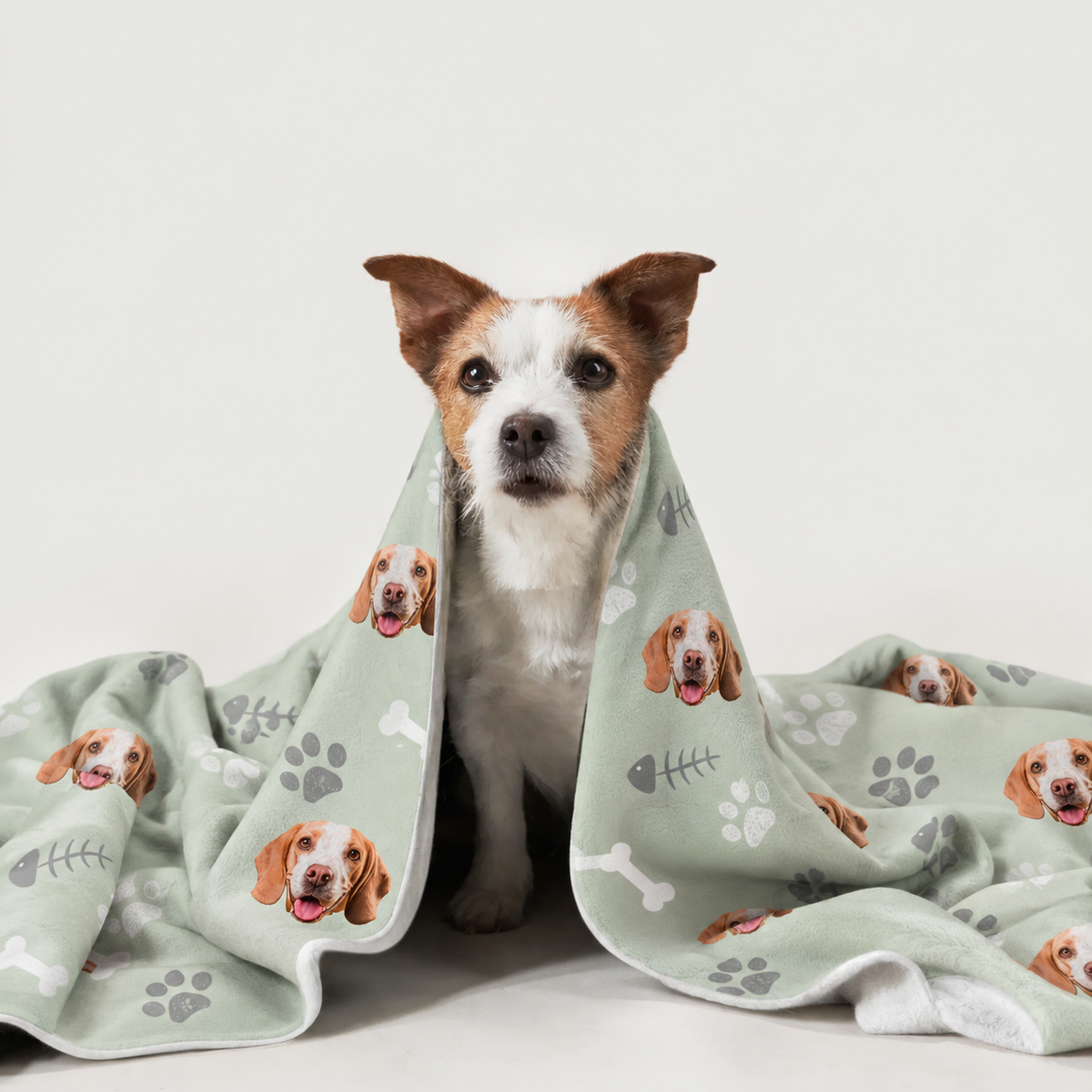 Hund eingehüllt in eine personalisierte Decke mit Hundemotiven auf grünem Hintergrund.