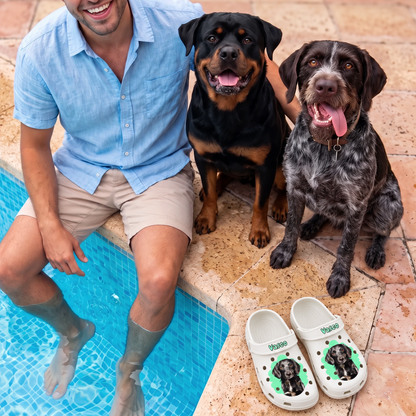 Person sitzt neben zwei Hunden am Pool, personalisierte weiße Clogs mit Haustierportrait daneben.